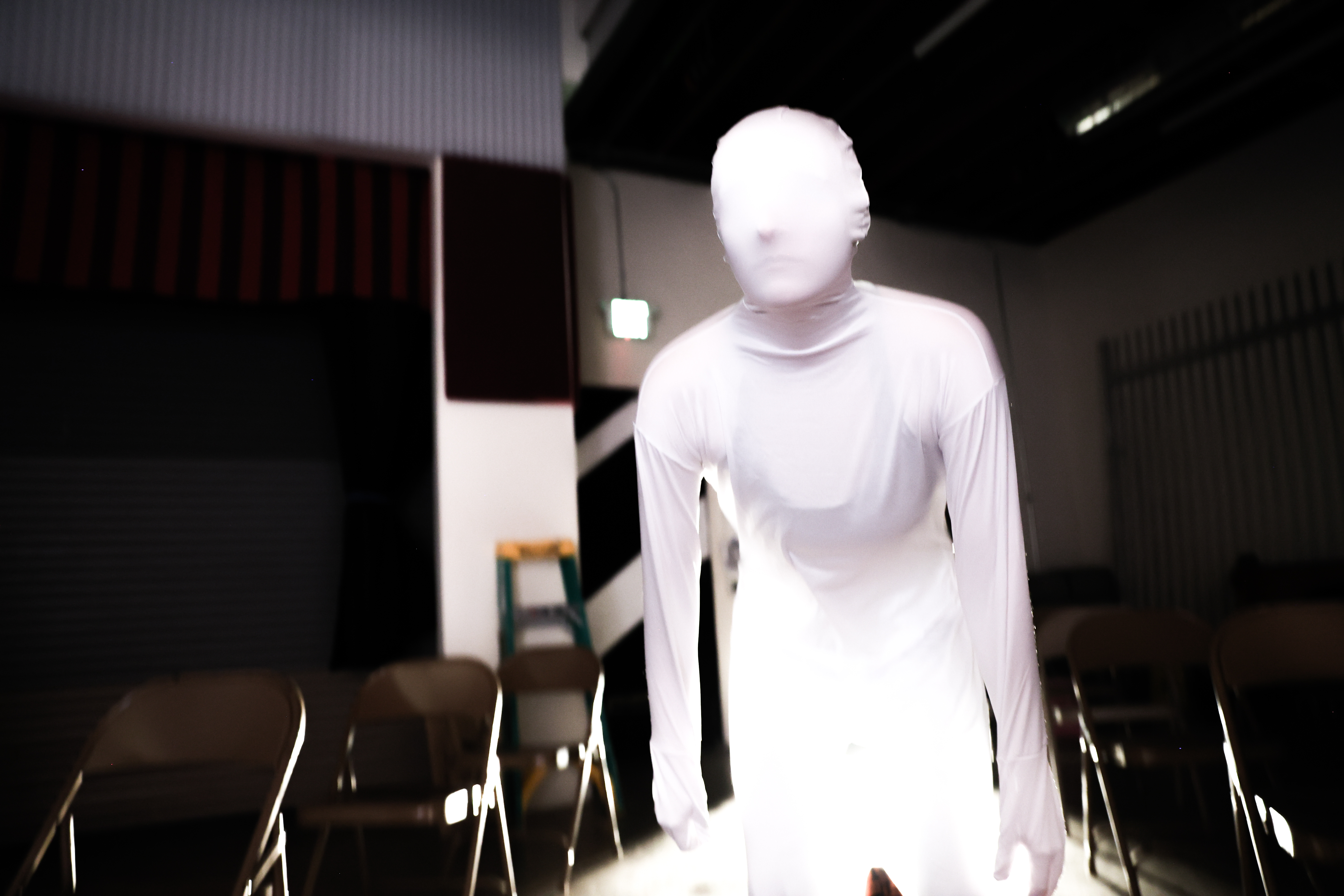 Anna in a white morphsuit, hunched over with a blank look.
